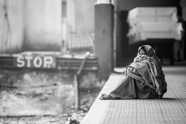 A woman wrapped in a shawl, sitting on a platform in India.