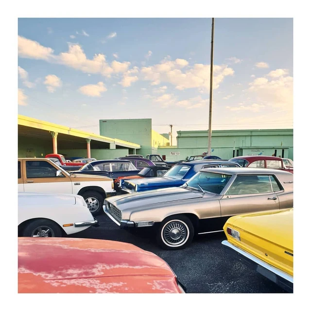 Colourful vintage cars parked outside pale green buildings beneath a cloudy sky.